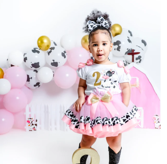 Child in a cow-themed outfit with balloons and decorations